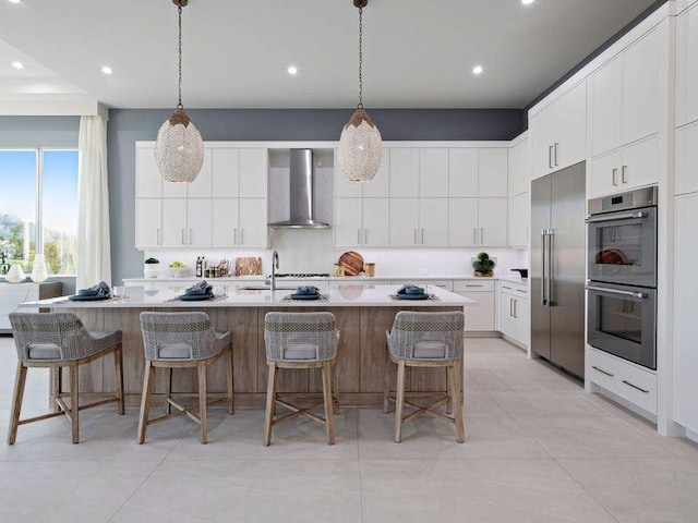 kitchen with wall chimney exhaust hood, white cabinetry, an island with sink, and stainless steel appliances