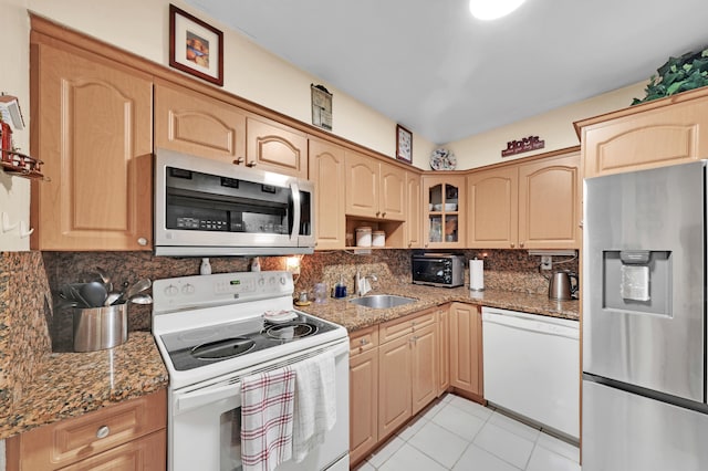 kitchen featuring sink, stainless steel appliances, dark stone countertops, light brown cabinetry, and light tile patterned floors