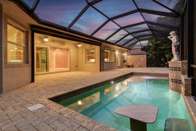 pool at dusk featuring glass enclosure, ceiling fan, and a patio area