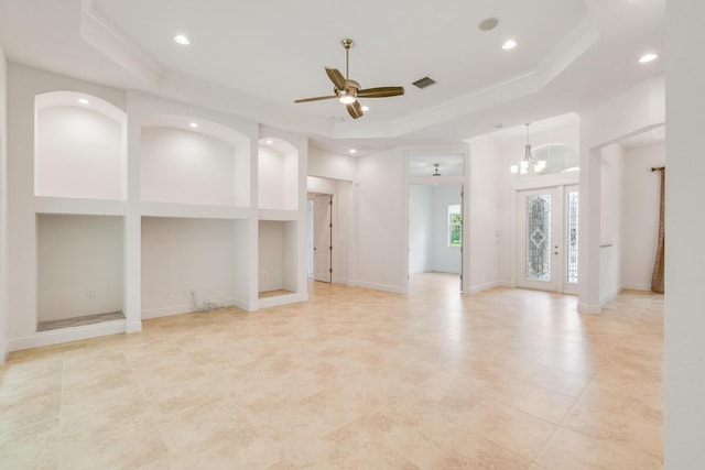 unfurnished living room with a tray ceiling, built in features, ceiling fan with notable chandelier, and ornamental molding