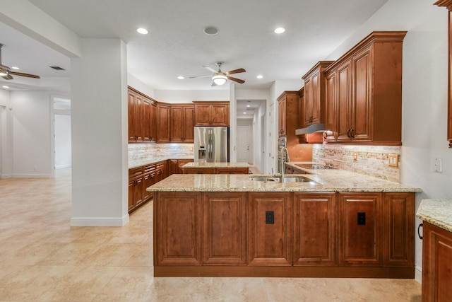 kitchen with sink, kitchen peninsula, light stone countertops, tasteful backsplash, and stainless steel fridge with ice dispenser