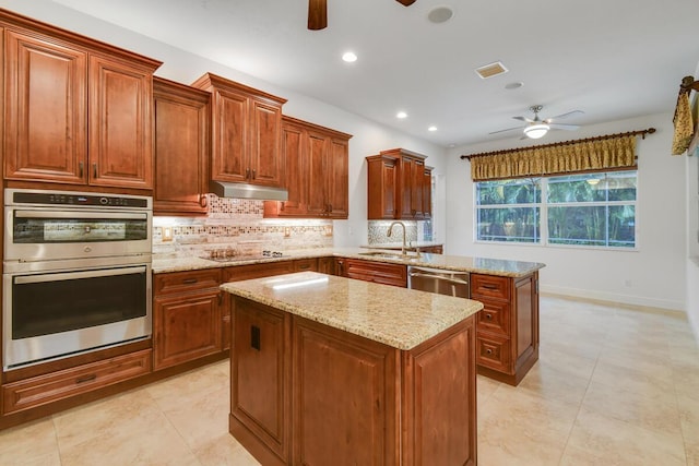 kitchen with light stone countertops, sink, stainless steel appliances, backsplash, and a kitchen island