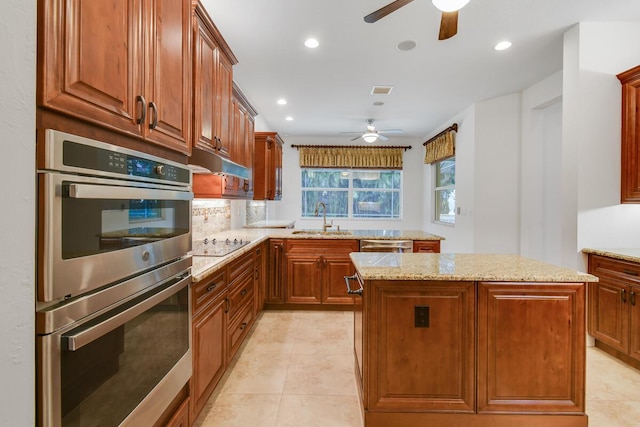 kitchen featuring sink, light stone countertops, black electric cooktop, double oven, and a kitchen island