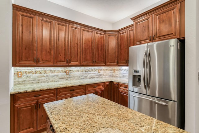 kitchen featuring backsplash, stainless steel fridge, and light stone counters