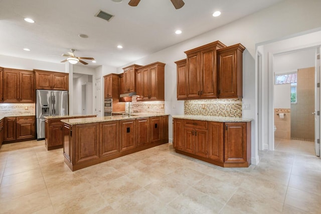 kitchen featuring a center island with sink, ceiling fan, light stone countertops, tasteful backsplash, and stainless steel appliances