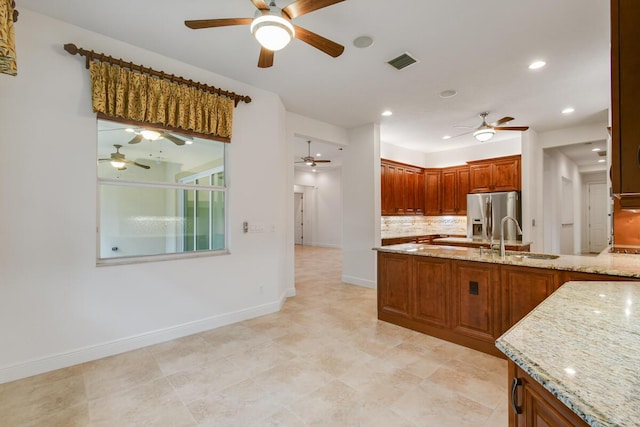 kitchen featuring light stone countertops, stainless steel fridge with ice dispenser, decorative backsplash, and sink