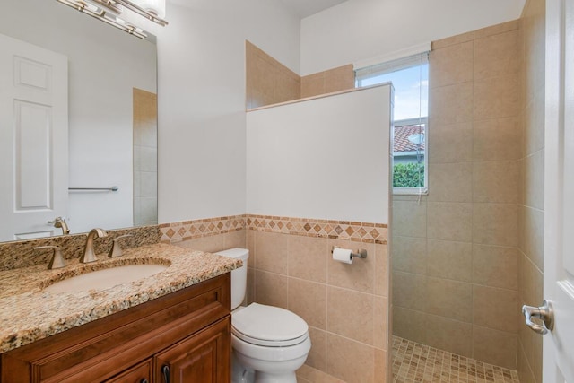 bathroom featuring tiled shower, vanity, tile walls, and toilet