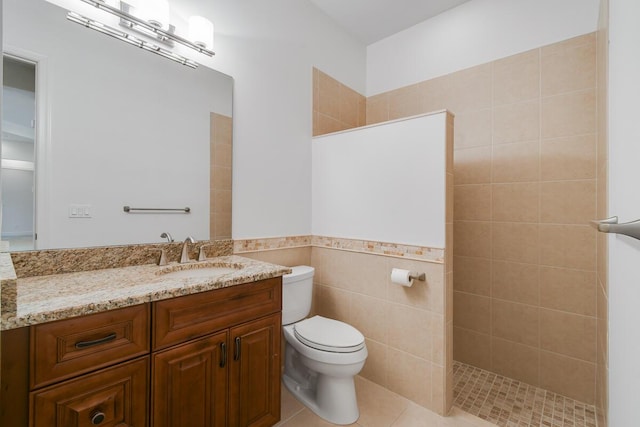 bathroom with tile patterned flooring, toilet, tiled shower, vanity, and tile walls