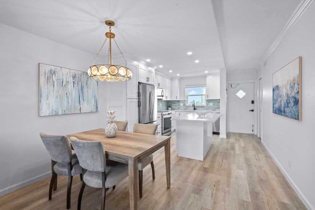 dining room with sink, light wood-type flooring, crown molding, and a notable chandelier