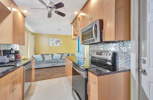 kitchen with backsplash, ceiling fan, dark stone countertops, light hardwood / wood-style floors, and stainless steel appliances