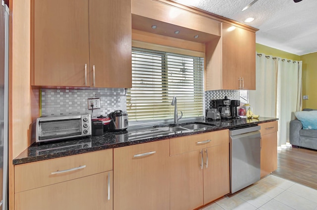 kitchen with backsplash, sink, stainless steel dishwasher, dark stone countertops, and a textured ceiling