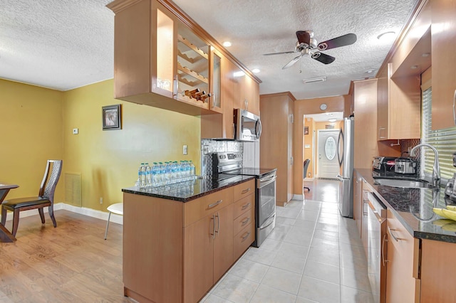 kitchen featuring dark stone counters, sink, ceiling fan, a textured ceiling, and stainless steel appliances