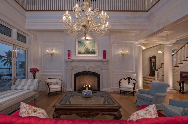 living room with an inviting chandelier, hardwood / wood-style floors, a towering ceiling, a fireplace, and ornamental molding