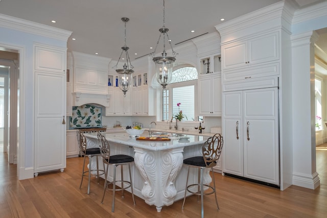 kitchen with white cabinets, light hardwood / wood-style floors, a kitchen island with sink, and crown molding