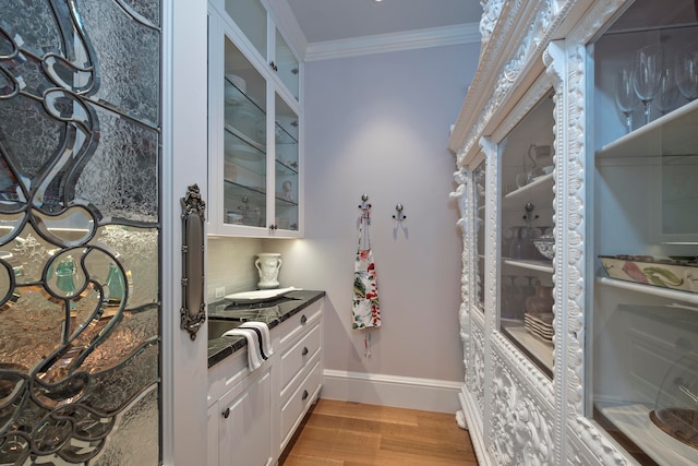 bar with decorative backsplash, light wood-type flooring, white cabinetry, and ornamental molding