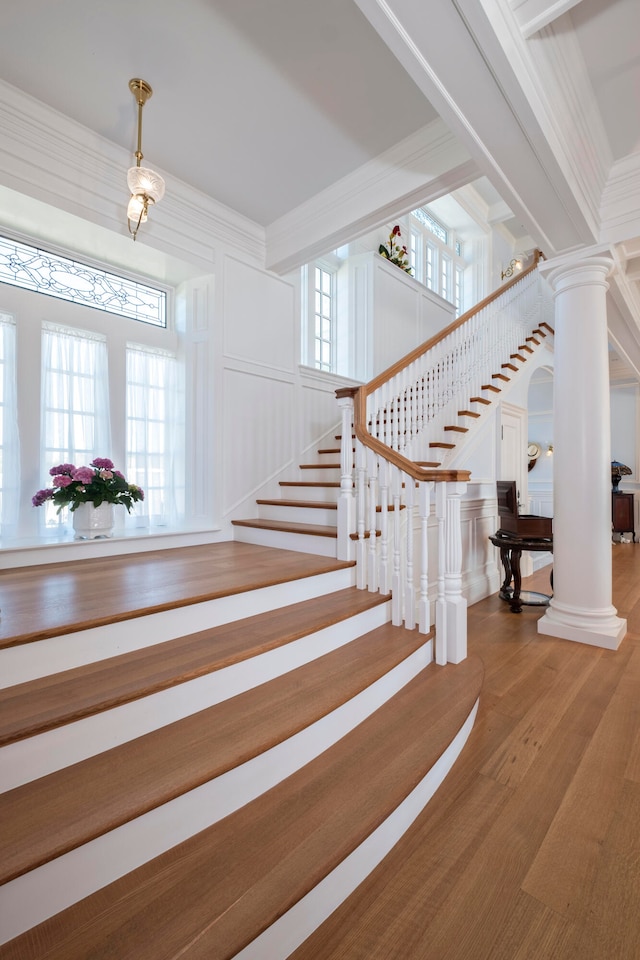 stairs featuring hardwood / wood-style floors, ornate columns, and crown molding