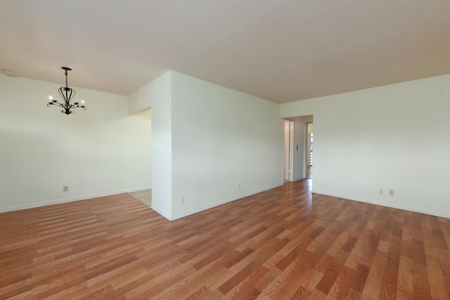 unfurnished room with light hardwood / wood-style flooring, a textured ceiling, and an inviting chandelier