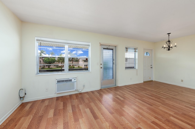 unfurnished living room with light hardwood / wood-style floors, a wall mounted air conditioner, and a notable chandelier