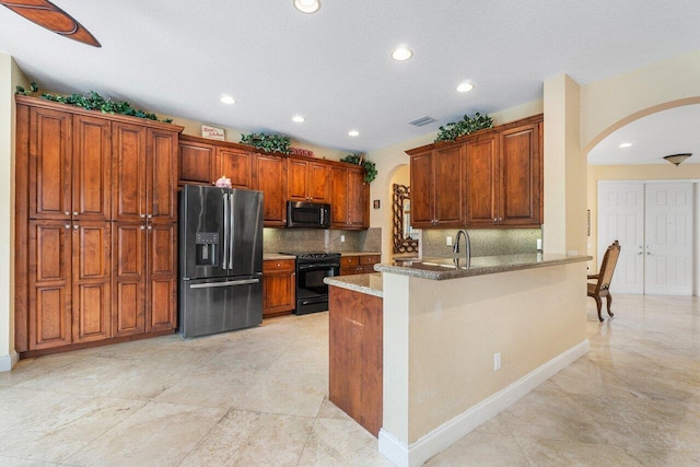 kitchen with kitchen peninsula, appliances with stainless steel finishes, decorative backsplash, a textured ceiling, and dark stone countertops