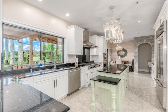 kitchen with wall chimney exhaust hood, stainless steel appliances, sink, white cabinets, and a center island