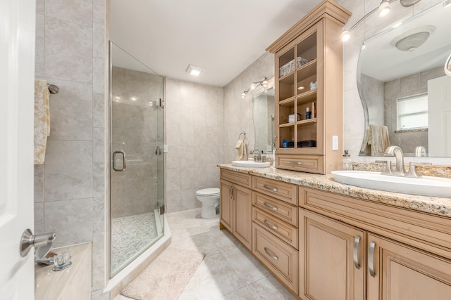 bathroom featuring tile patterned floors, toilet, a shower with door, vanity, and tile walls