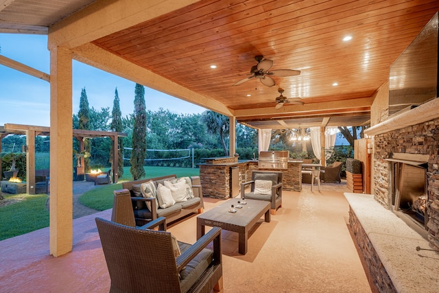 patio terrace at dusk with an outdoor living space with a fireplace, a grill, ceiling fan, and exterior kitchen