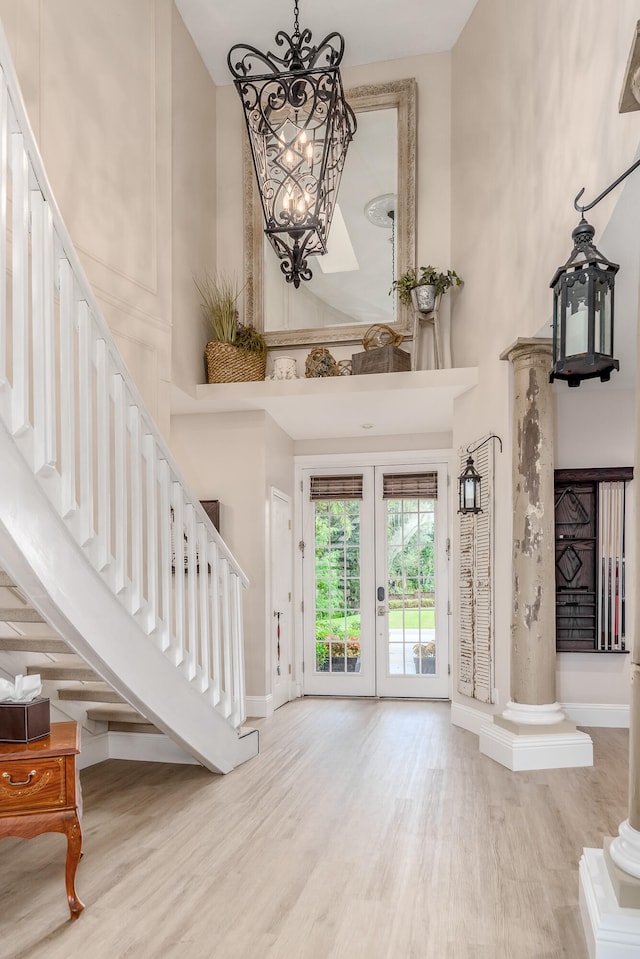 entryway featuring french doors, a towering ceiling, ornate columns, an inviting chandelier, and light hardwood / wood-style flooring