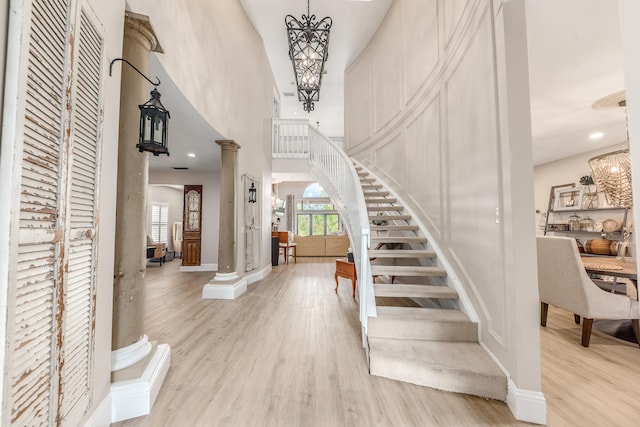 entryway featuring a towering ceiling, light wood-type flooring, decorative columns, and a notable chandelier