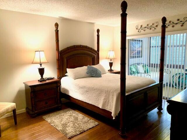 bedroom with access to exterior, a textured ceiling, and hardwood / wood-style flooring