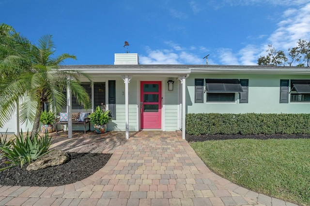 view of front of property with a porch, a chimney, and stucco siding