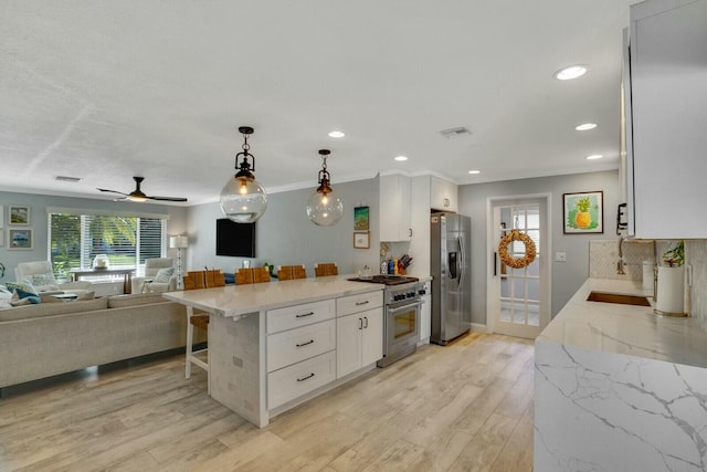 kitchen with a breakfast bar area, light stone counters, pendant lighting, stainless steel appliances, and white cabinets