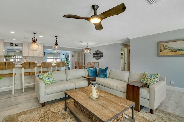 living area with light wood-type flooring, crown molding, baseboards, and recessed lighting