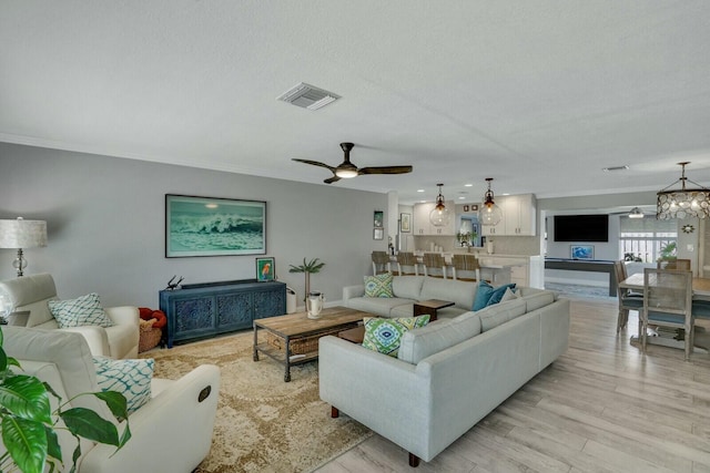 living room with ceiling fan with notable chandelier, ornamental molding, visible vents, and light wood-style floors