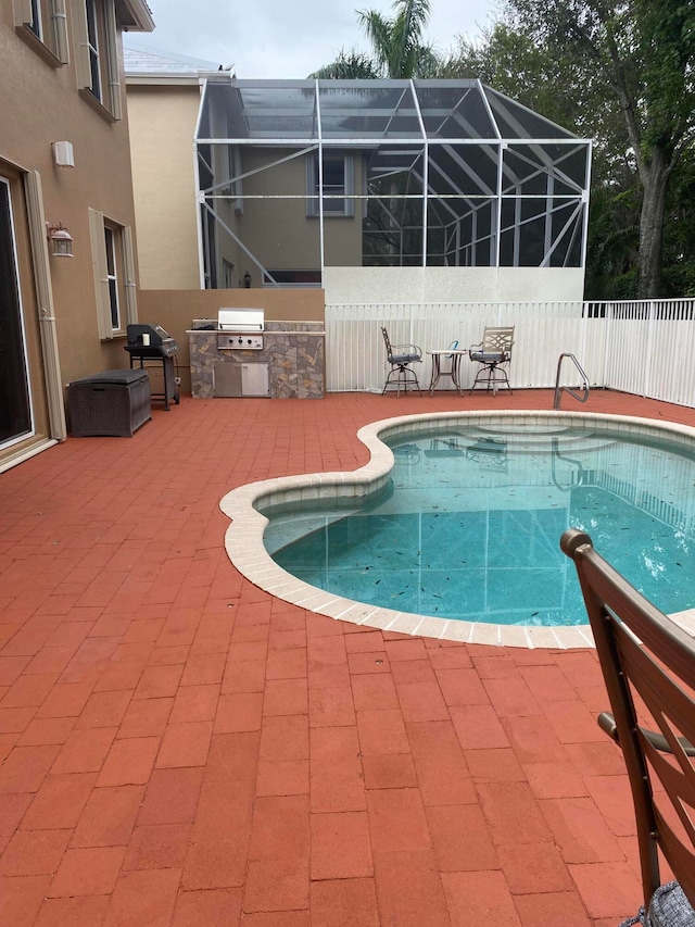 view of swimming pool featuring an outdoor kitchen, a lanai, a patio, and grilling area