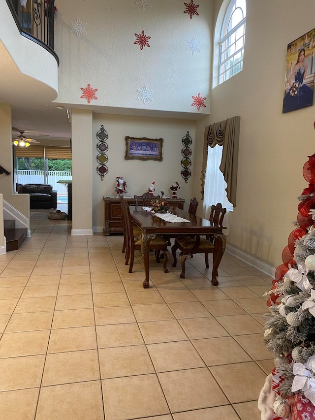 tiled dining space with ceiling fan, plenty of natural light, and a towering ceiling