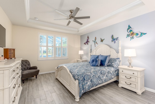 bedroom with light wood-type flooring, a tray ceiling, ceiling fan, and crown molding