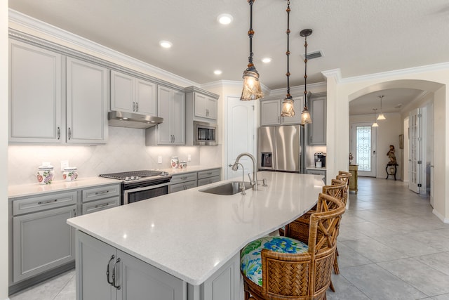 kitchen with gray cabinetry, a center island with sink, sink, appliances with stainless steel finishes, and decorative light fixtures