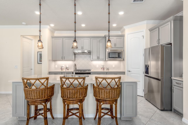 kitchen with pendant lighting, stainless steel appliances, gray cabinetry, and an island with sink