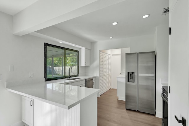 kitchen with sink, kitchen peninsula, light wood-type flooring, white cabinetry, and stainless steel appliances