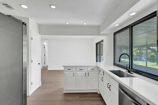 kitchen with sink, white cabinetry, wood-type flooring, stainless steel dishwasher, and a barn door