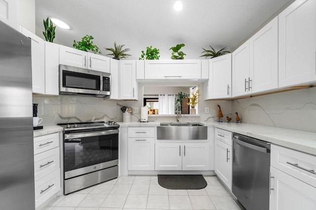 kitchen with light stone counters, stainless steel appliances, sink, light tile patterned floors, and white cabinets