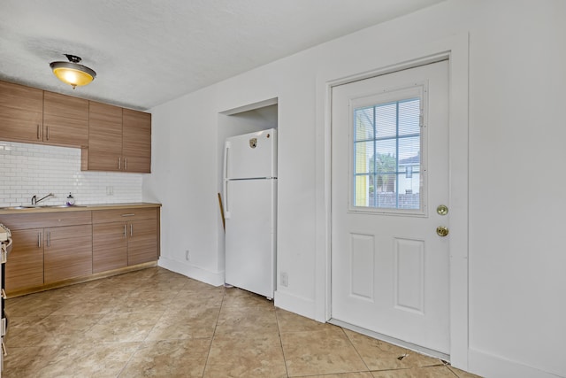 kitchen featuring white refrigerator, sink, light tile patterned floors, a textured ceiling, and tasteful backsplash