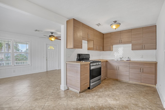 kitchen with decorative backsplash, sink, ceiling fan, and stainless steel range with gas stovetop