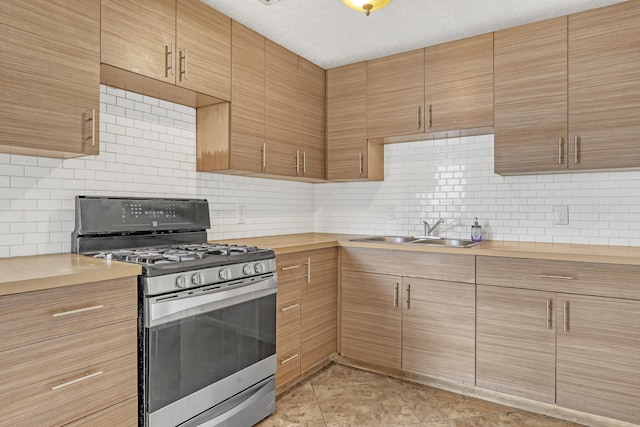 kitchen with decorative backsplash, a textured ceiling, sink, light tile patterned floors, and stainless steel gas stove