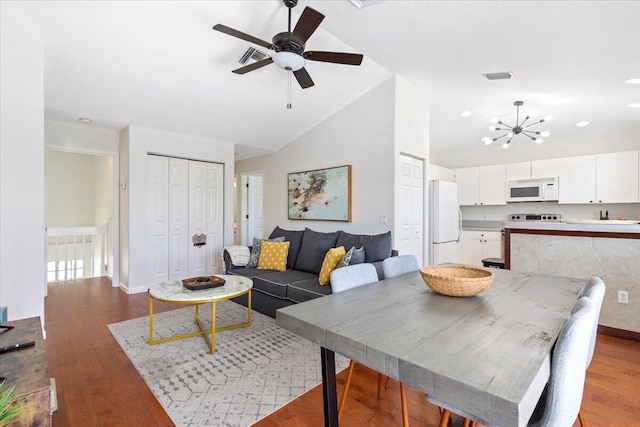 dining area featuring ceiling fan with notable chandelier, vaulted ceiling, and light hardwood / wood-style flooring