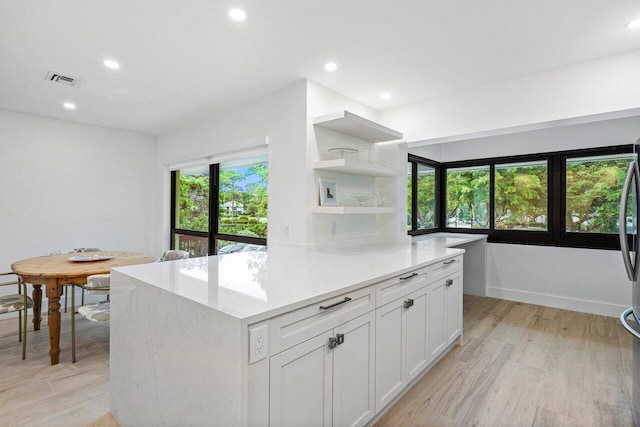 kitchen with white cabinets, light stone countertops, light hardwood / wood-style floors, and a wealth of natural light