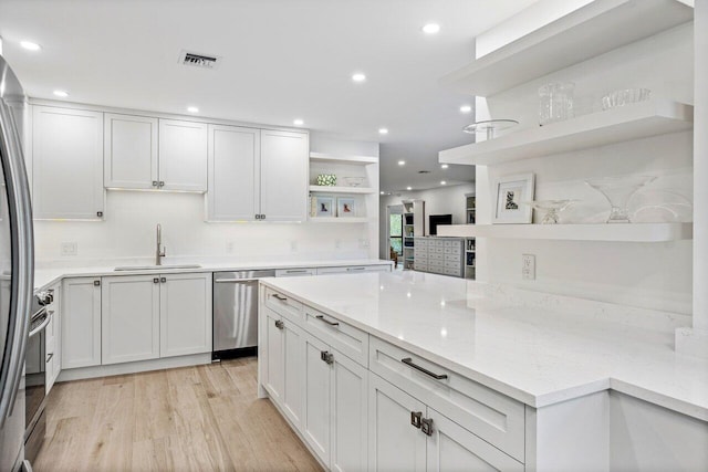 kitchen featuring white cabinetry, sink, light stone countertops, appliances with stainless steel finishes, and light wood-type flooring