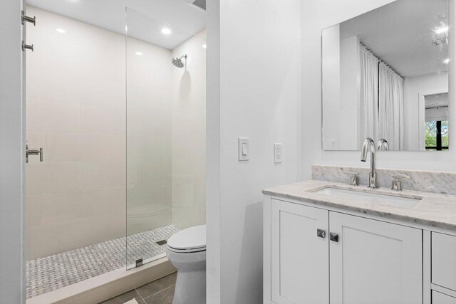 bathroom with tile patterned flooring, vanity, toilet, and tiled shower