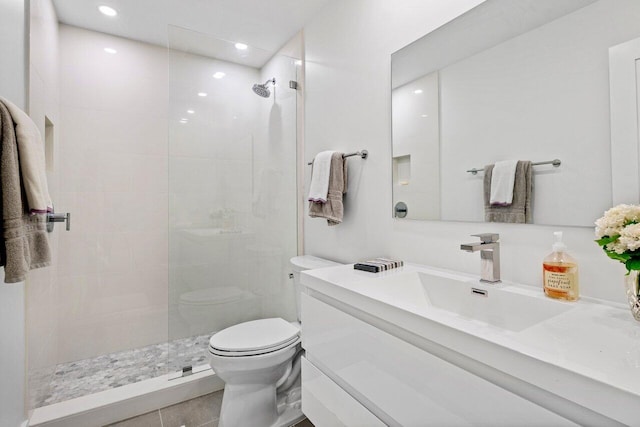 bathroom with tile patterned flooring, vanity, toilet, and tiled shower