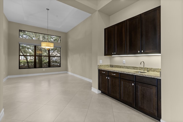 kitchen with pendant lighting, sink, dark brown cabinets, a tray ceiling, and light stone countertops